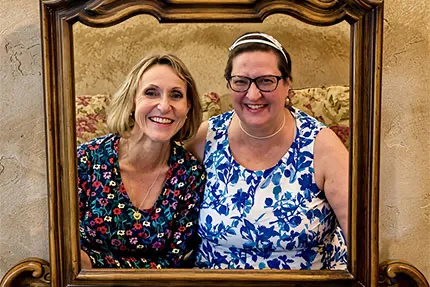 Kasia and Beata sitting on a couch and holding a picture frame as they pose inside